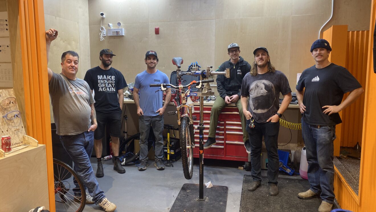 A group of bike mechanics gathered around a bike repair stand.