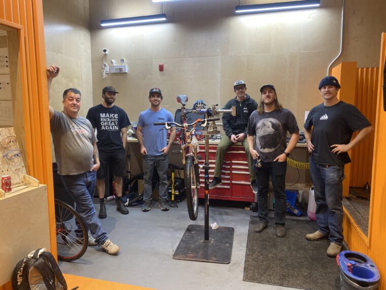 A group of bike mechanics gathered around a bike repair stand.