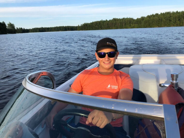 Smiling woman in sunglasses on boat in scenic lake setting.
